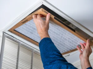 Person installing a new return air filter into a ceiling grille during routine HVAC maintenance. Best for blogs about how to change an HVAC filter, return air filter replacement, dirty air filter symptoms, indoor air quality, airflow problems, and HVAC maintenance tips.