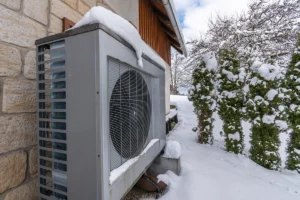 Outdoor heat pump unit installed beside a home in snowy winter conditions. Best for blogs about heat pump in winter, heat pump defrost cycle, winter HVAC performance, and cold-weather heat pump operation.