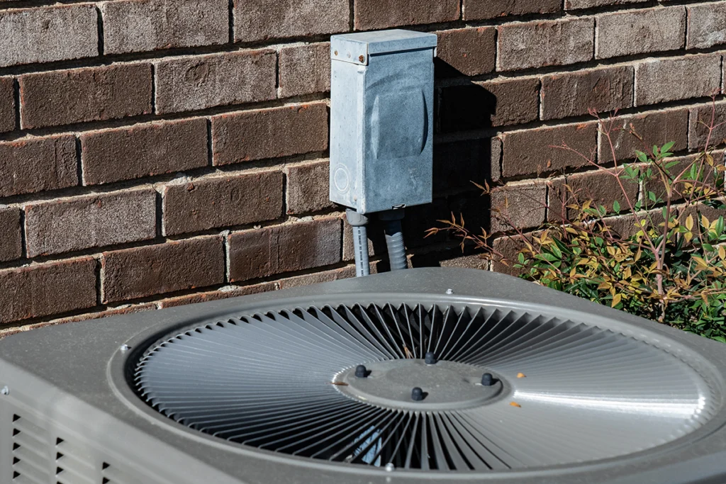 Outdoor residential air conditioning condenser unit installed beside a brick wall.